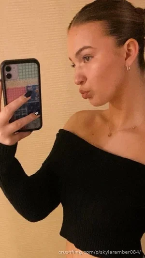 Woman in black off-shoulder top taking mirror selfie indoors.