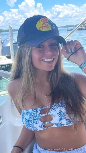 Woman with long hair wearing blue patterned top and cap, smiling on a boat.