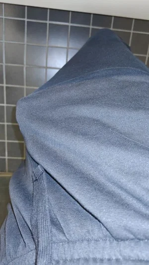 Person in blue hoodie, hood up, against tiled wall.