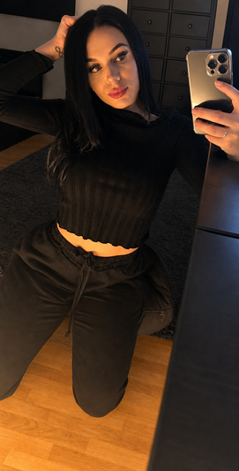 Brunette woman in black crop top and pants taking selfie.