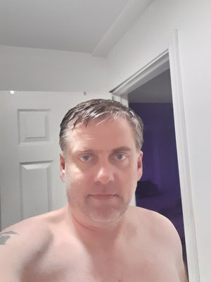 Shirtless man taking selfie indoors near white door.