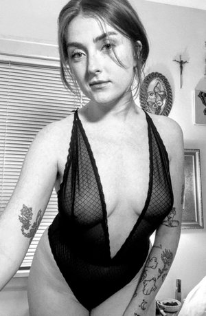 Curvy brunette in sheer black lace bodysuit indoors.