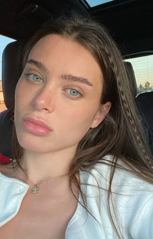 Woman with long brown hair in white top taking car selfie.