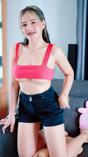 Woman with blonde hair in pink top and denim shorts indoors.