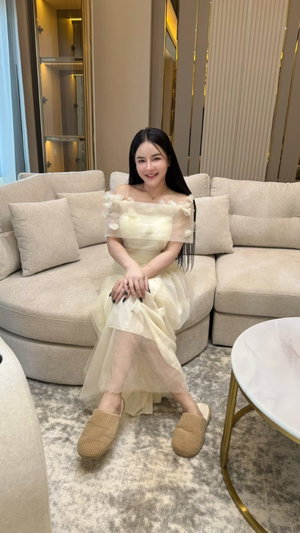 Woman with long dark hair in cream dress on beige sofa.