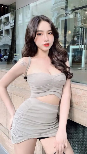 Asian woman with long hair in beige dress posing outdoors.