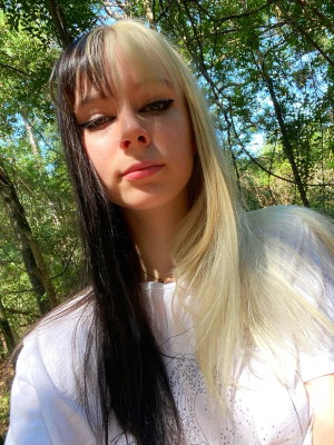 Woman with split black and blonde hair in white t-shirt outdoors.