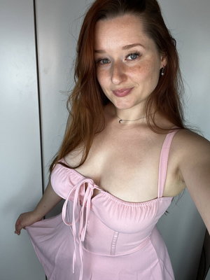 Woman with red hair in pink dress posing indoors.