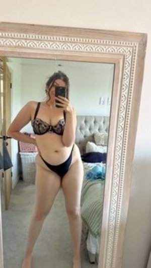 Woman in black lingerie taking mirror selfie in bedroom.