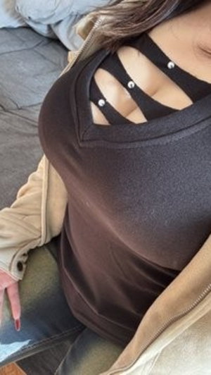 Woman in black cutout top and beige jacket, sitting indoors on gray surface.