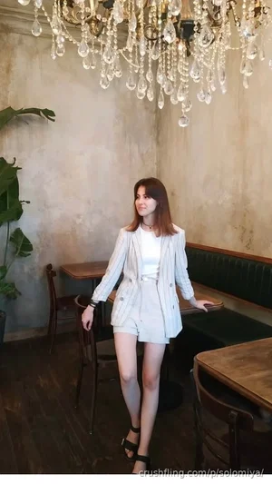 Woman in white blazer and shorts standing in a restaurant with chandelier and green booth.