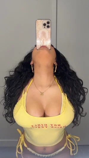 Woman with curly hair in yellow top and white underwear, taking mirror selfie indoors.