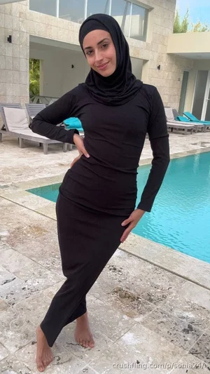 Woman in black full-body swimwear and hijab posing by poolside.