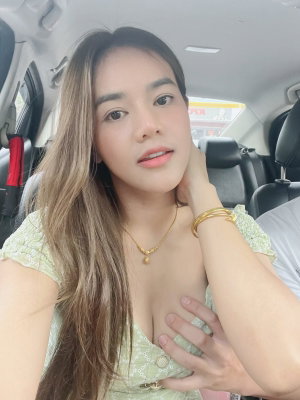 Woman with long hair in green top taking selfie in car.