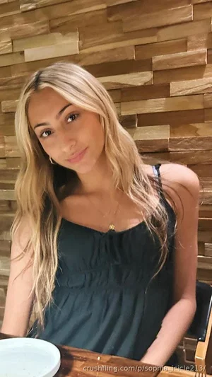 Woman with blonde hair in a dark green top, sitting at a wooden table indoors.