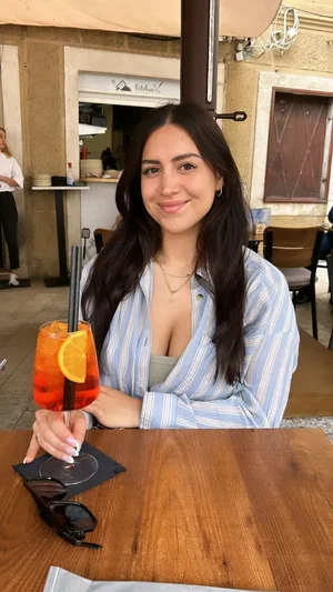 Woman with long dark hair in striped shirt holding drink at outdoor table.