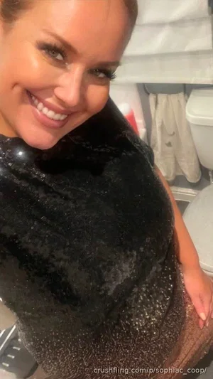 Woman in black sequined dress smiling in bathroom selfie.