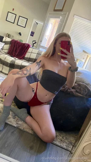 Woman with blonde hair and tattoos wears black bandeau and red underwear, kneeling on floor in