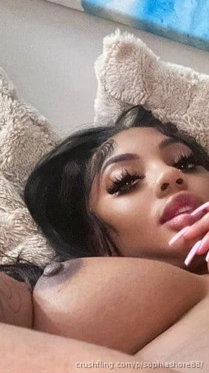 Woman with dark hair and makeup lying on a fluffy surface, wearing a furry headband.