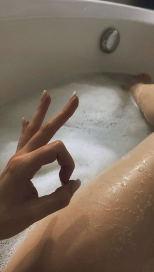 Woman in bubble bath, hand visible, leg partially shown, indoor setting.