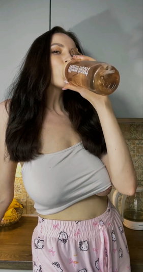 Woman with long dark hair drinking from bottle in kitchen.