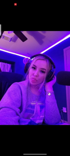 Woman with blonde hair wearing headphones and a gray sweatshirt in a room with purple LED lights.