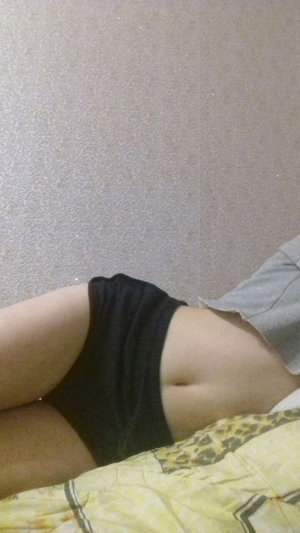 Slim woman in black shorts and gray crop top on bed.