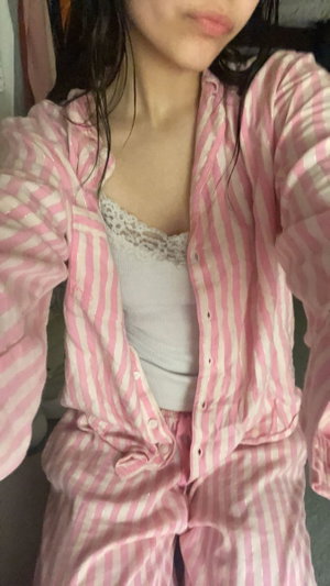 Slim Asian woman in open pink striped pajamas, indoor selfie.