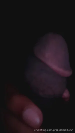 Close-up of a hand holding a small, dark, mushroom-shaped object in low light.