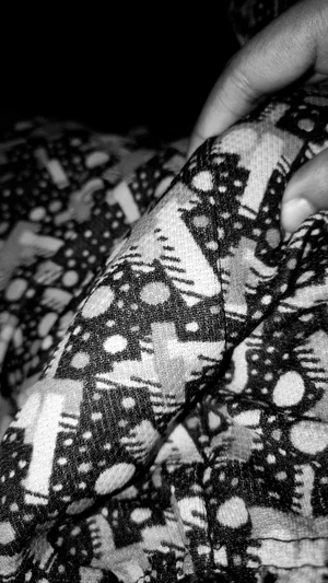Close-up of patterned fabric, hand holding material, dark background.