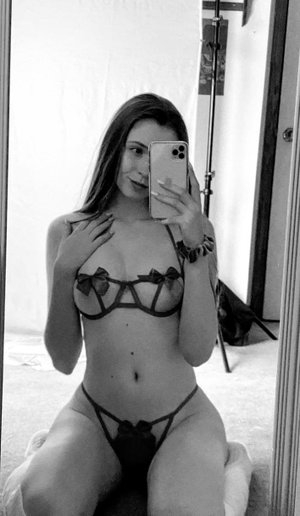 Brunette woman in black strappy lingerie, mirror selfie indoors.