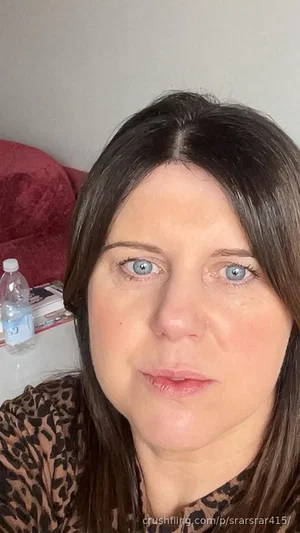 Woman with dark hair and blue eyes wearing leopard print top, indoors.
