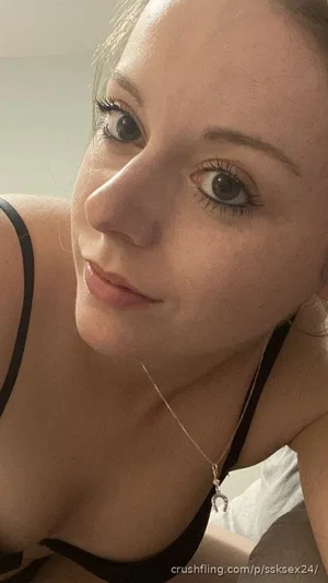 Woman in black bra, close-up selfie, indoor setting, soft lighting.