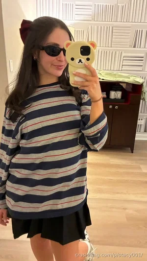 Woman in striped sweater and black skirt takes mirror selfie indoors.