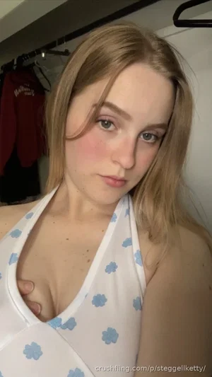 Woman with blonde hair in a white floral top, indoors, facing camera.