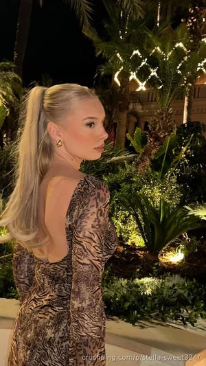 Blonde woman in a sheer leopard-print dress, standing outdoors at night near palm trees.