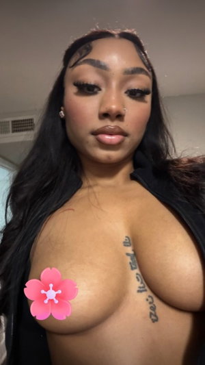 Black woman with long hair in open black top showing cleavage indoors.