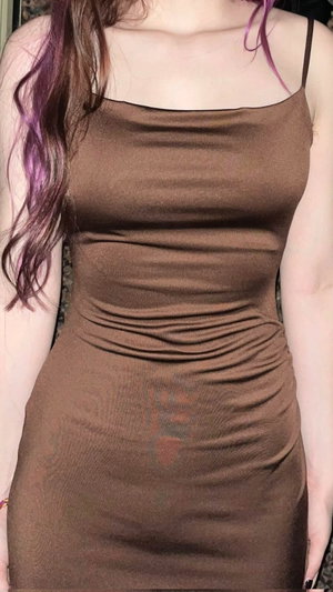 Woman with purple-streaked hair in brown ruched dress.