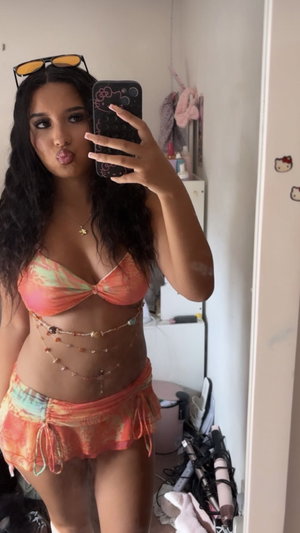 Dark-haired woman in bikini taking mirror selfie indoors.