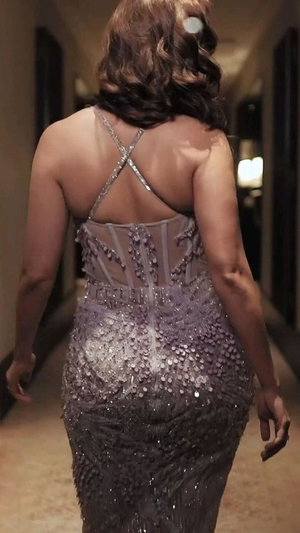 Woman in sparkling sequined gown walking in hallway from behind.