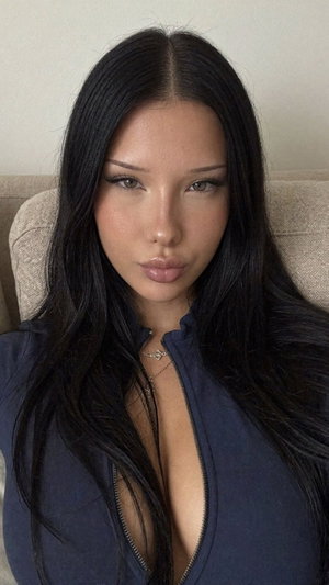 Woman with long black hair in a dark blue zip-up top, sitting indoors.