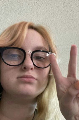 Blonde woman with glasses making peace sign indoors.