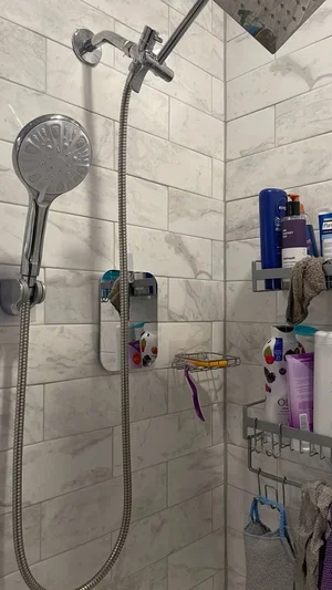 Shower with marble tiles, handheld showerhead, and toiletries on racks.