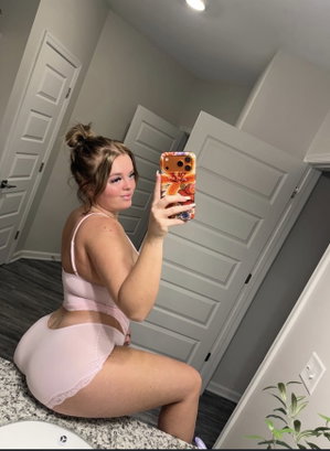 Curvy woman in pink lingerie taking a mirror selfie in a bathroom.