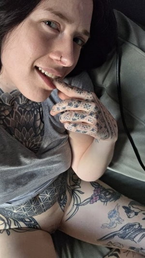 Tattooed woman with dark hair smiling indoors.