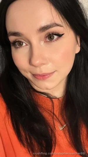 Woman with long black hair and makeup wearing an orange top, close-up selfie.