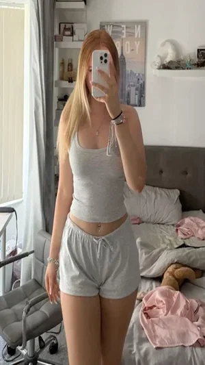Blonde woman in gray tank top and shorts in bedroom.