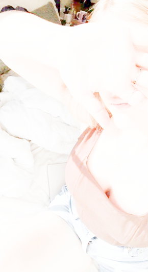 Blonde woman in pink top on bed.