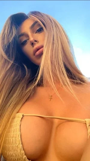 Woman with long blonde hair in a yellow top, outdoors under blue sky.