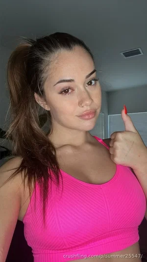Woman in bright pink sports bra, giving thumbs up, indoor setting.